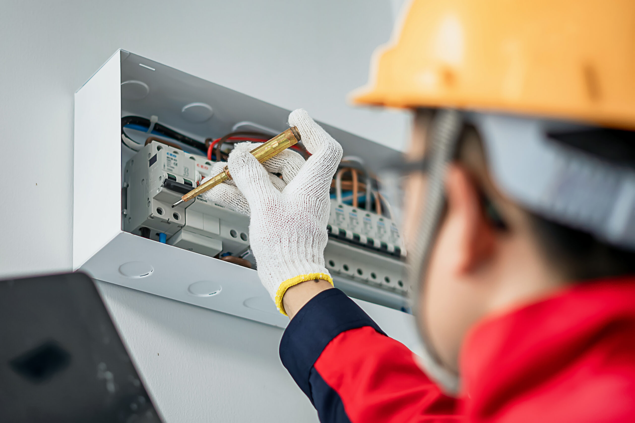 Asian electrical engineer wearing safety helmet inspecting home electrical system with tools and tablet at indoor building site